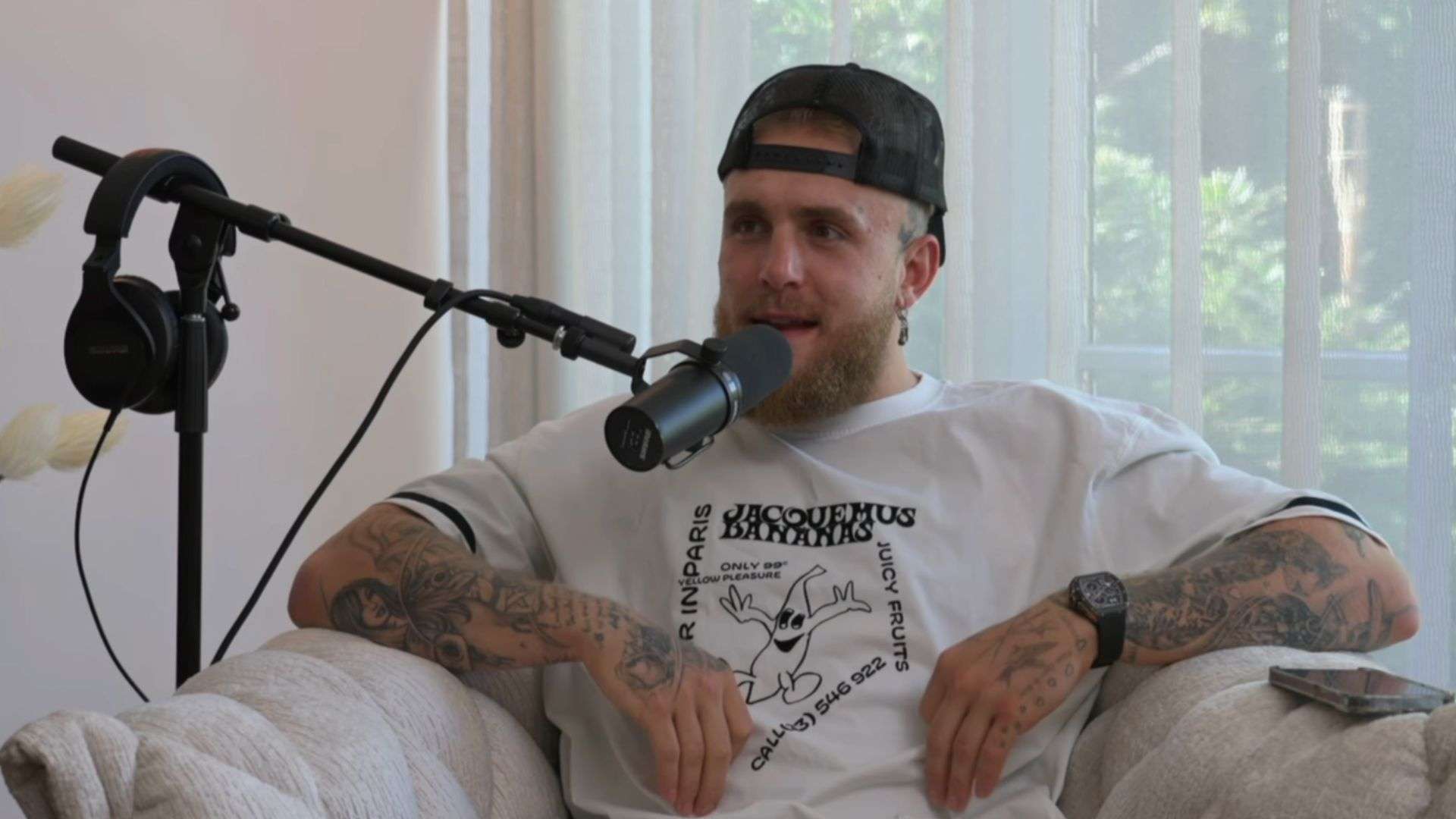 Jake Paul in white shirt talking into microphone while sat on couch