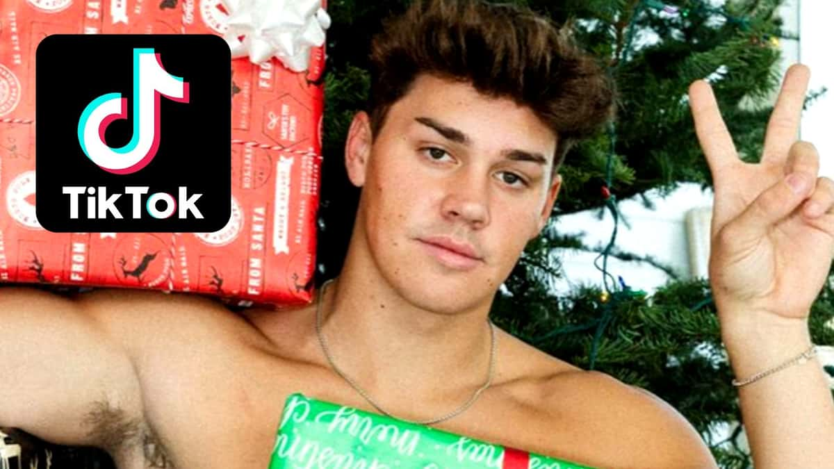 Noah Beck poses in front of a tree next to the TikTok logo