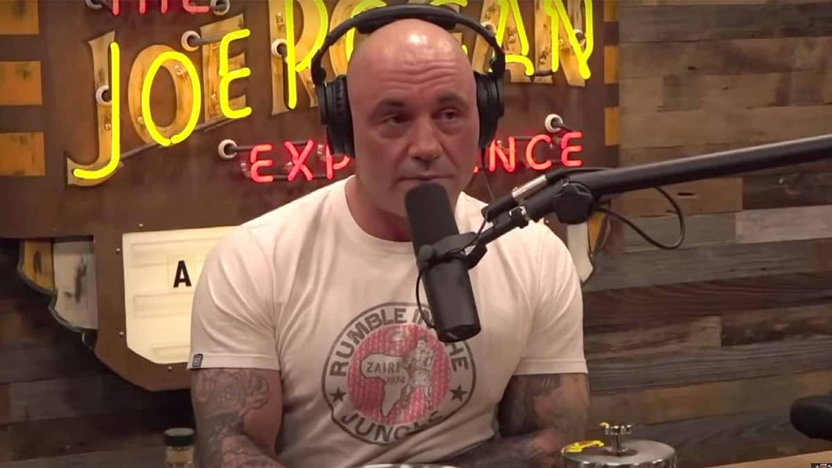 Joe Rogan talking into microphone wearing white shirt