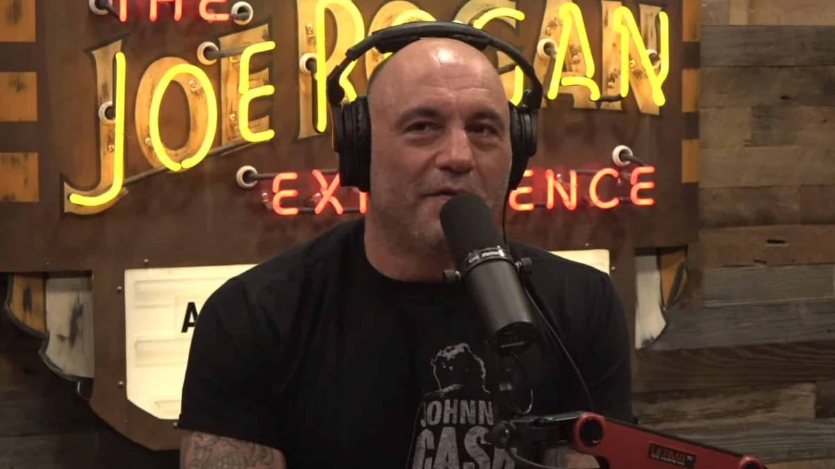 Joe Rogan looking skyward while smiling behind microphone