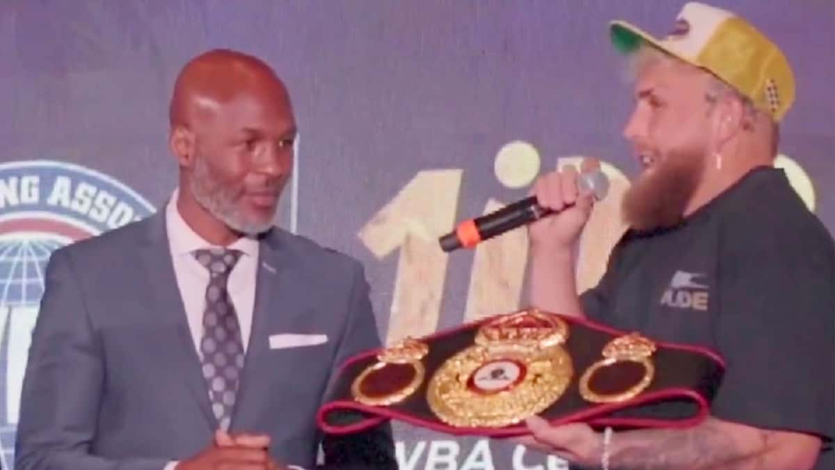 Jake Paul holding boxing title belt and mic next to bernard hopkins