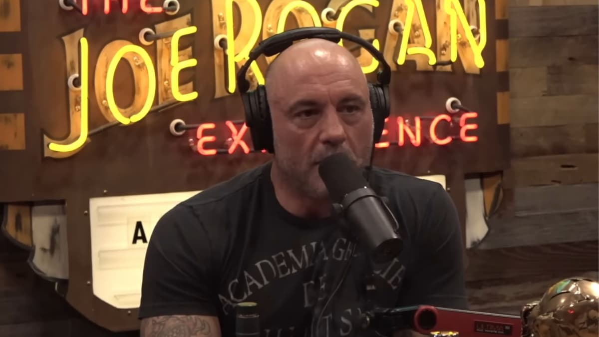 Joe Rogan talking into mic in black shirt on podcast set