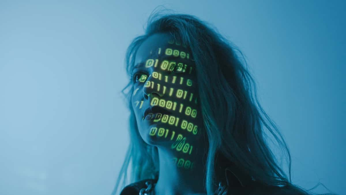 A woman on a blue background with green code projected on face