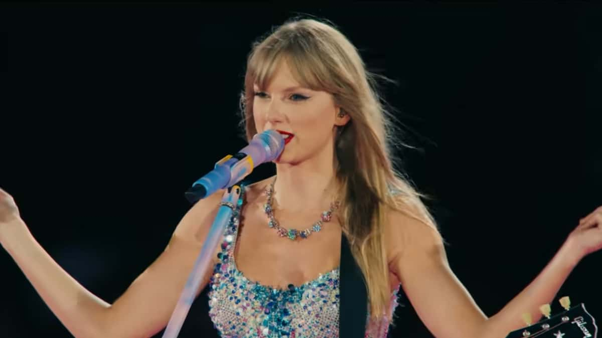 Taylor Swift performing onstage with an acoustic guitar at a concert.