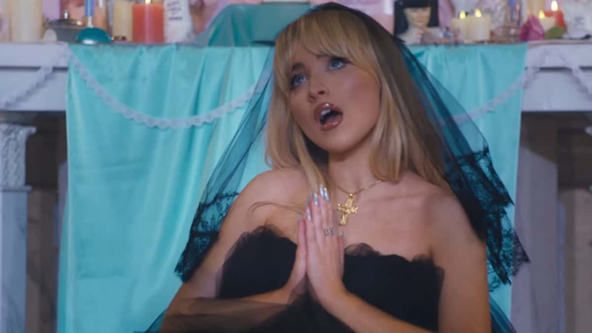 Sabrina Carpenter in a black veil and dress praying on a church altar