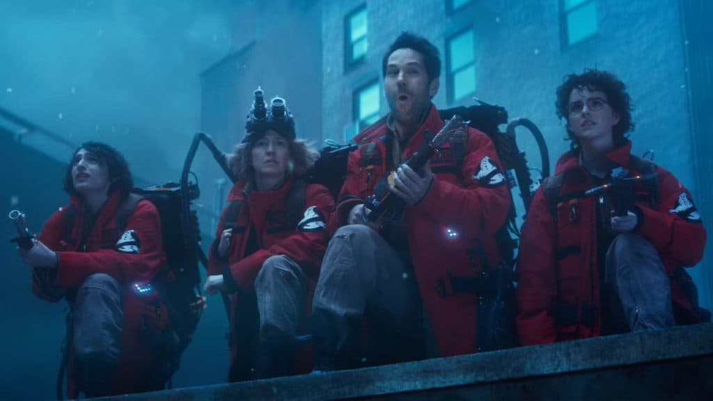 The cast of Ghostbusters: Afterlife stand on a rooftop in red uniforms