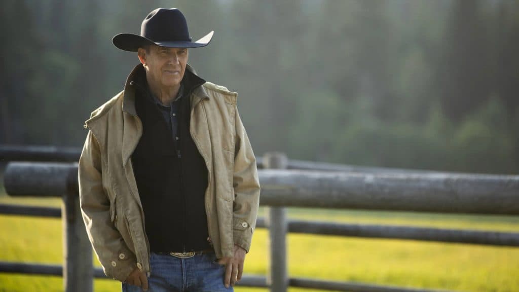 Kevin Costner as John Dutton in Yellowstone, wearing a cowboy hat and standing in the field