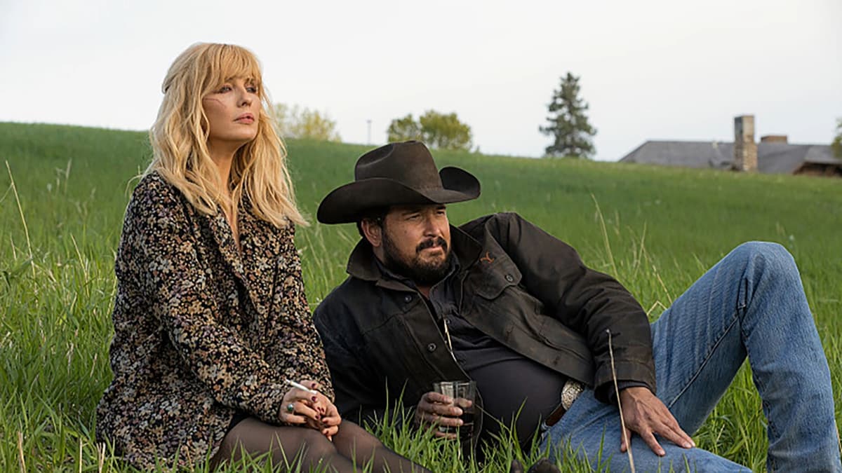 Kelly Reilly and Cole Hauser as Beth and Rip in Yellowstone, laying on the grass