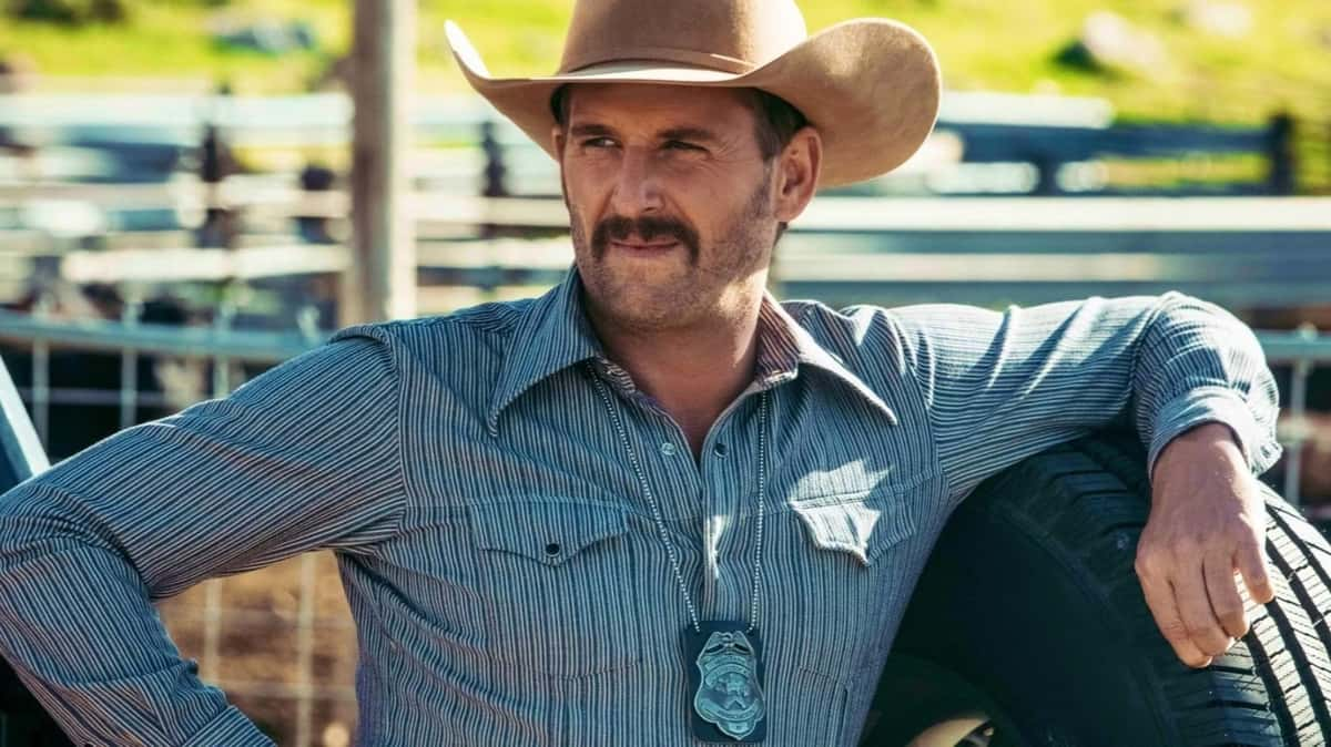 Josh Lucas as a young John Dutton in Yellowstone, leaning against a fence