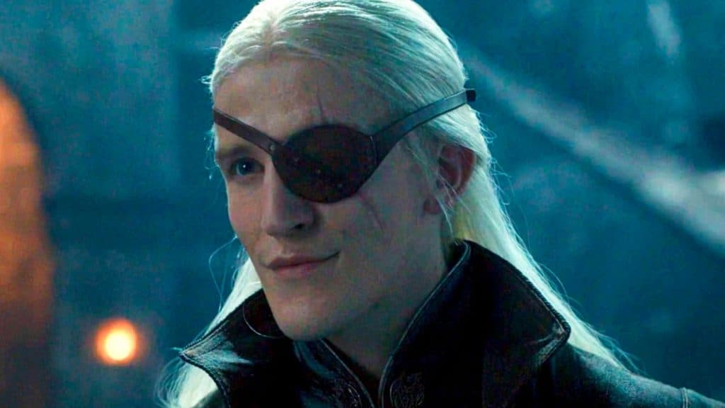 Aemond wears an eye patch and smirks across a drark room.