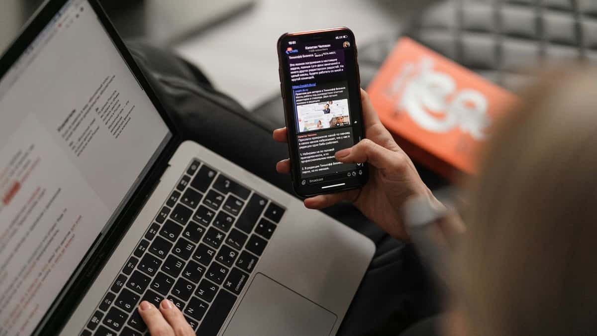 Person scrolling on phone while working on laptop