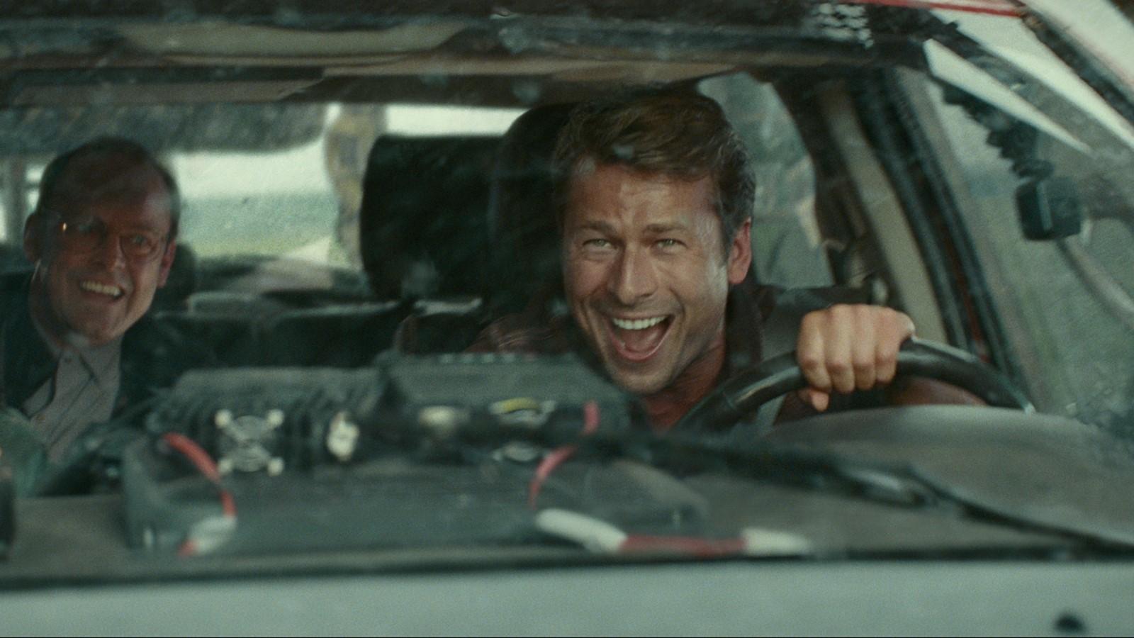 How to watch Twisters: Glen Powell sitting behind the wheel of a car and smiling