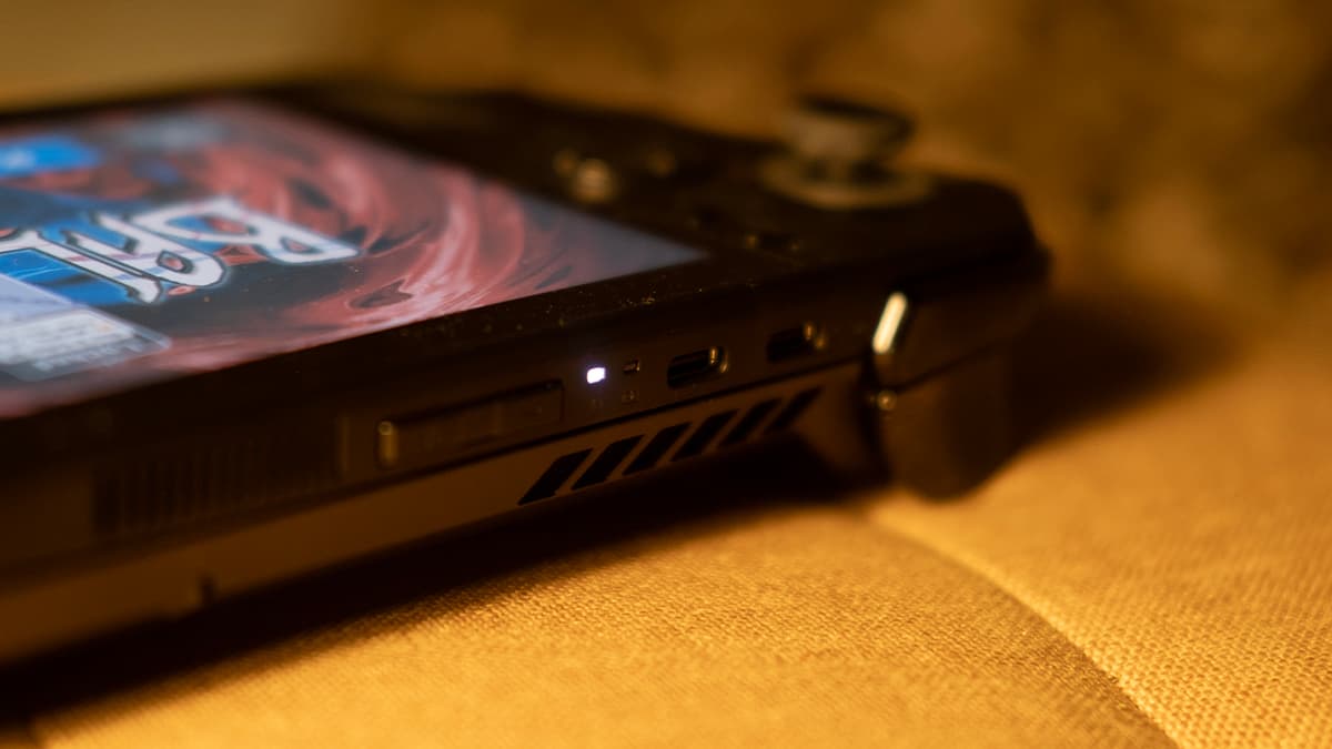 Asus ROG Ally X displaying Balatro, but the camera is focused on the two usb-c ports on the top, on a yellow cushion surface