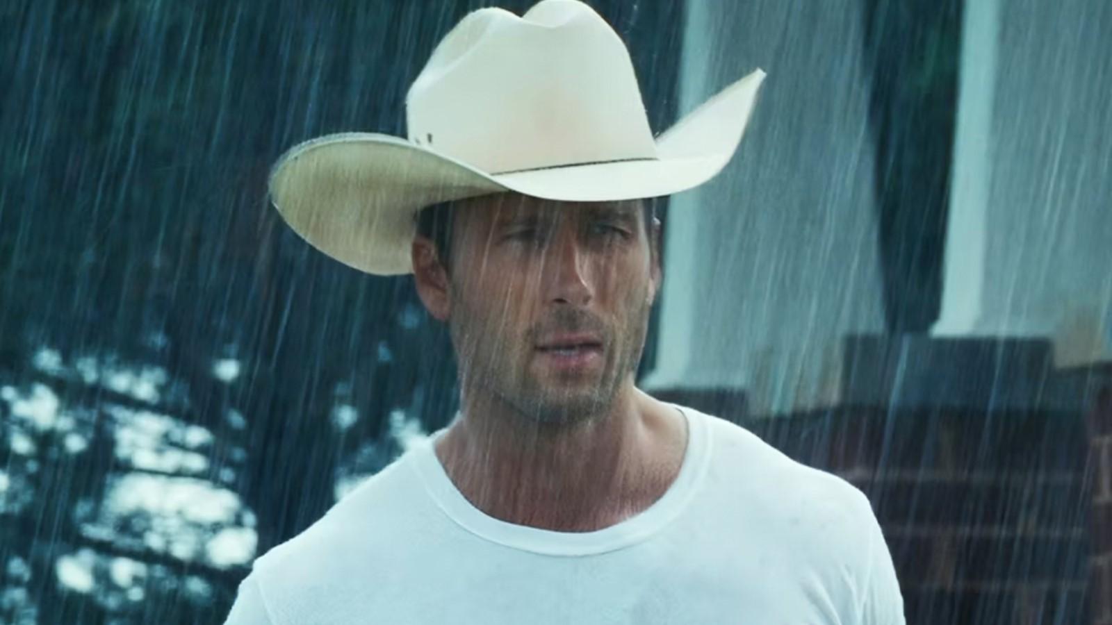 Glen Powell as Tyler Owens in Twisters, in the rain wearing a cowboy hat