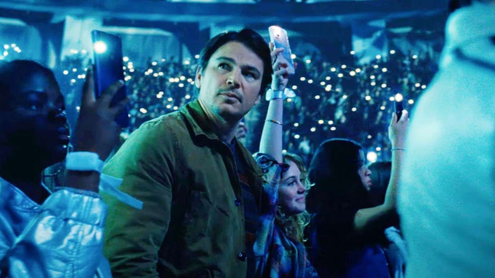 Josh Hartnett as Cooper in Trap, standing in a concert surrounded by a crowd and blue lights