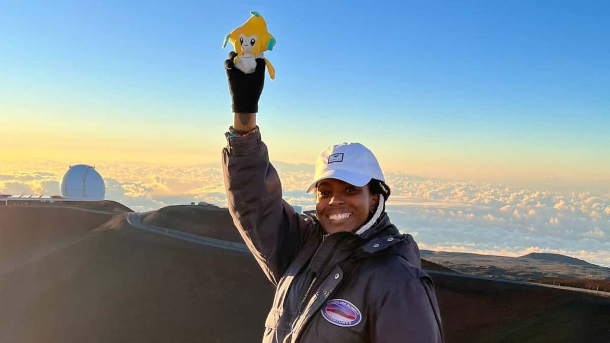 A Pokemon Go player stands at the top of a mountain, holding a Jirachi plush