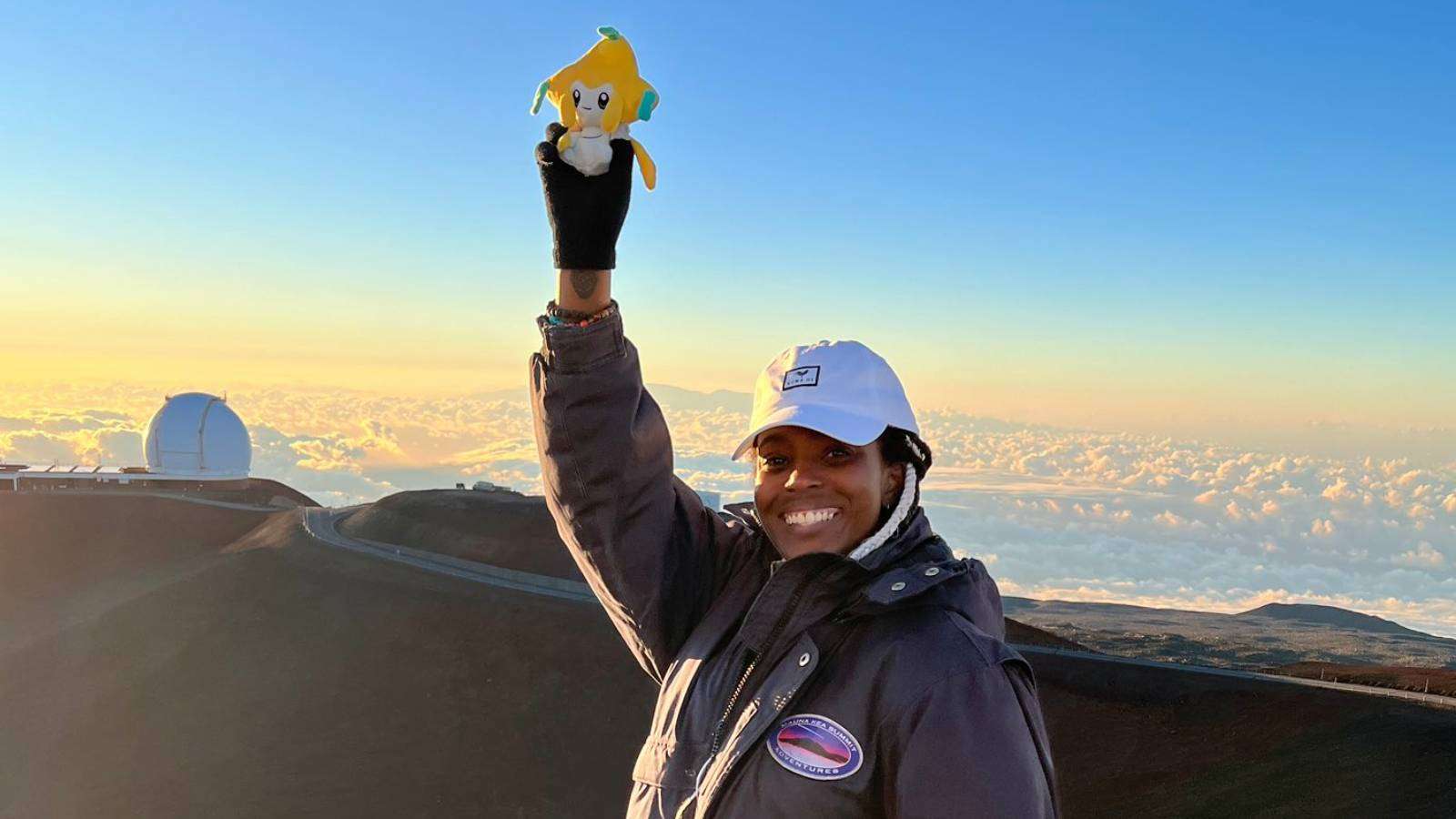 A Pokemon Go player stands at the top of a mountain, holding a Jirachi plush