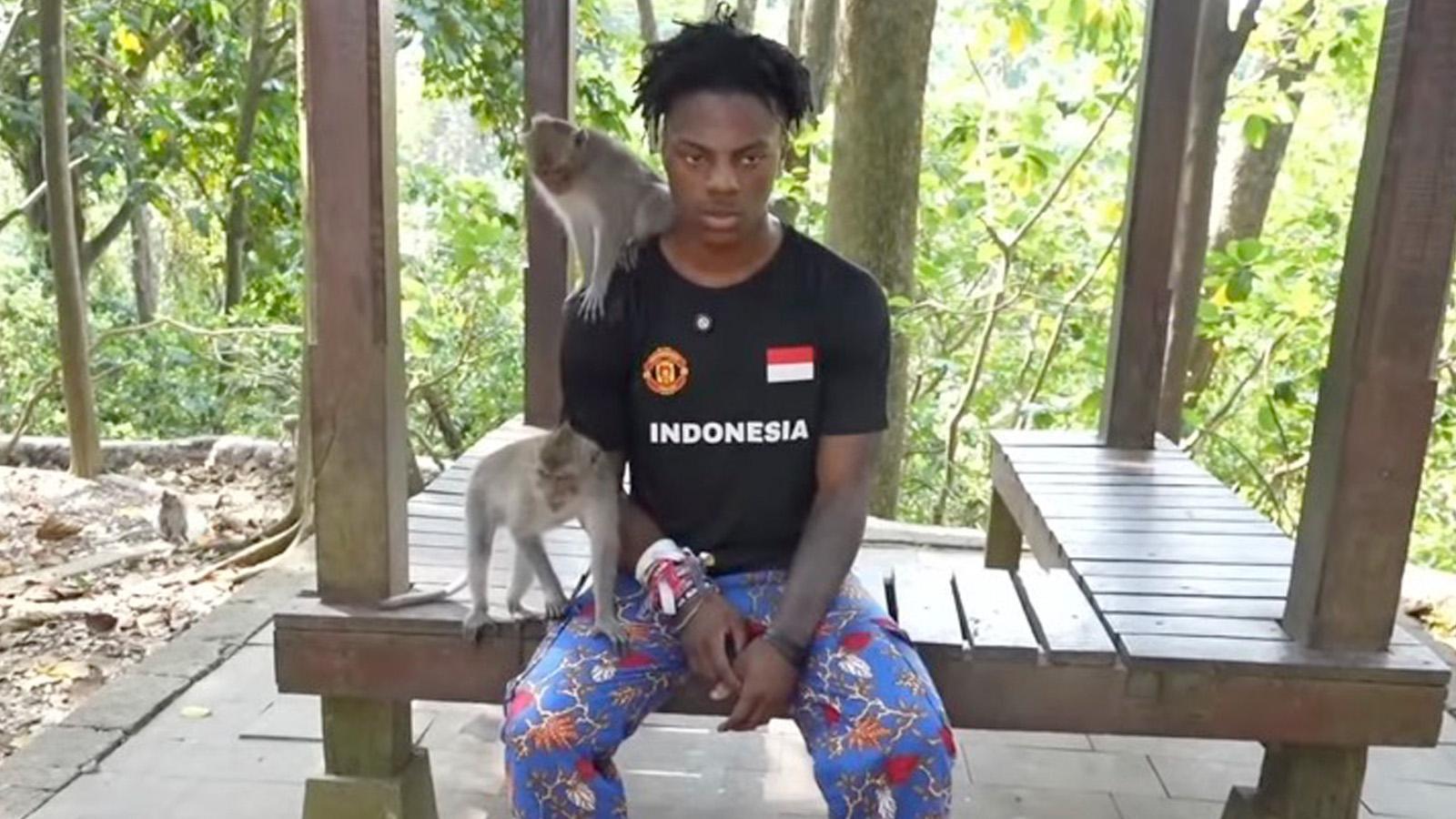 ishowspeed sitting on a bench with monkeys climbing on him