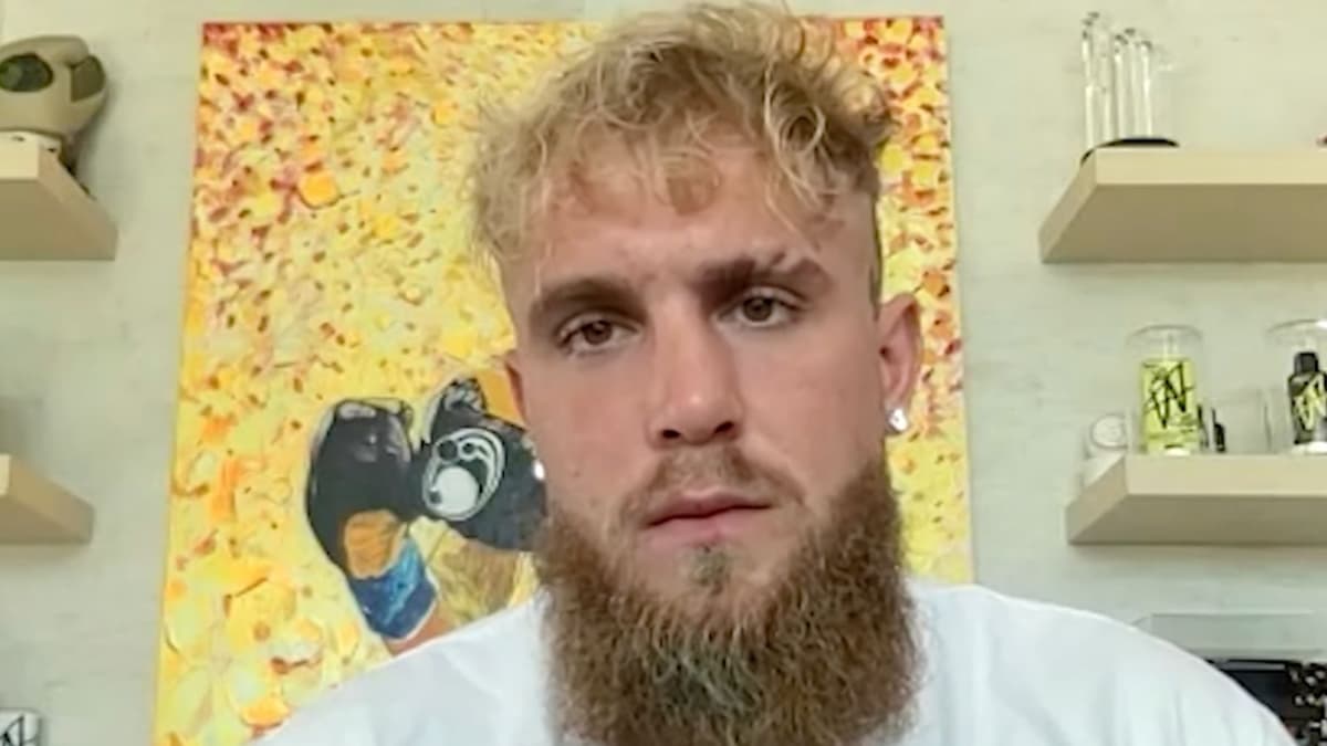 Jake Paul talking to camera in white t-shirt in front of yellow painting