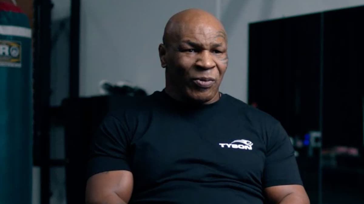 Mike Tyson sitting down talking to camera in black Tyson shirt