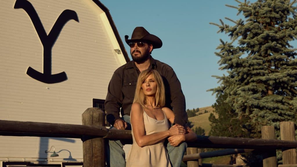 Yellowstone: Beth and Rip sitting by a fence with the Yellowstone logo in the background