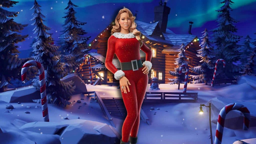 Mariah Carey, wearing a red and white Santa suit, posing in front of a log cabin