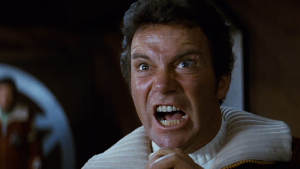 Captain James T. Kirk looks horrified as he holds a microphone