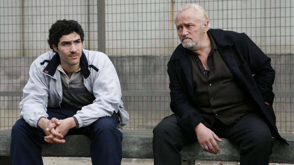 A young man and an older an sit on a bench looking glum