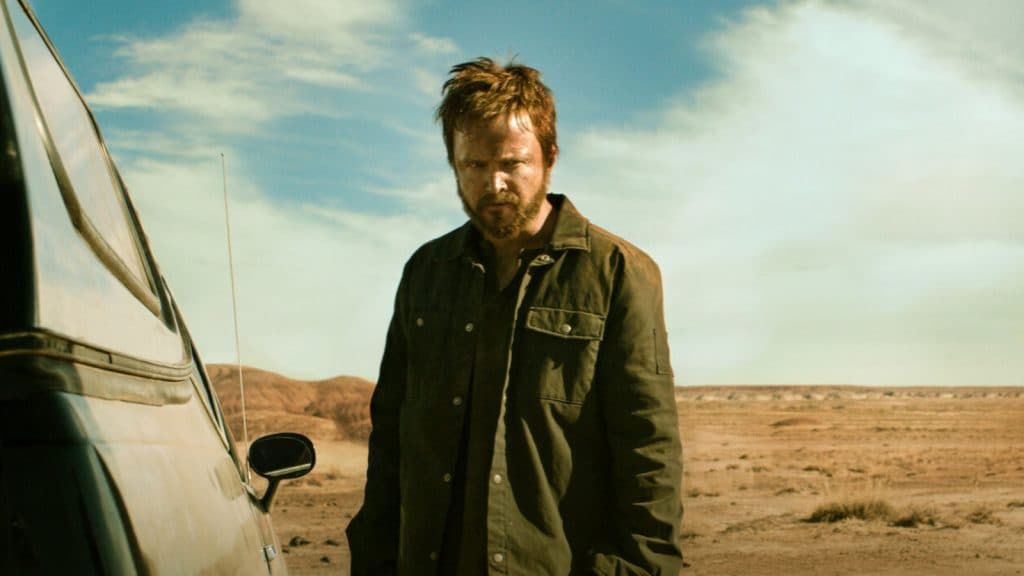 A disheveled Jesse Pinkman stands in a desert looking tired but determined.