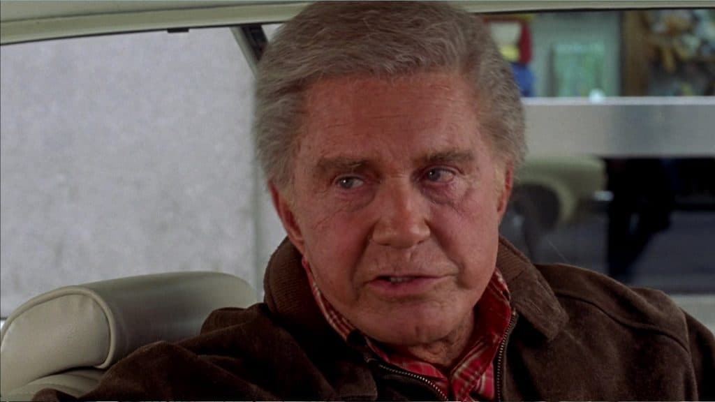 An older white man sits in a car with a concerned look on his face.