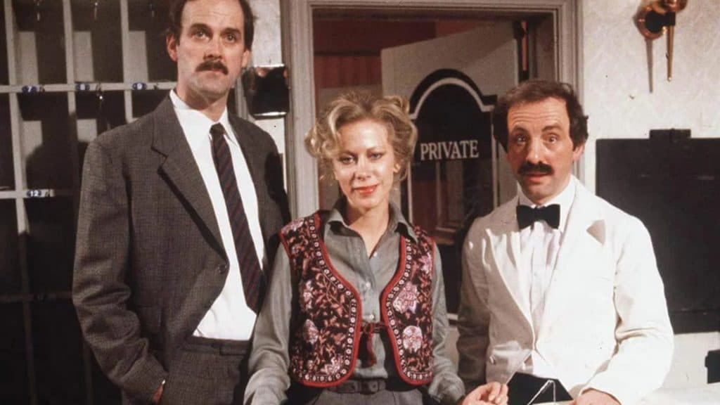 The staff of Fawlty Towers standing behind the front desk.