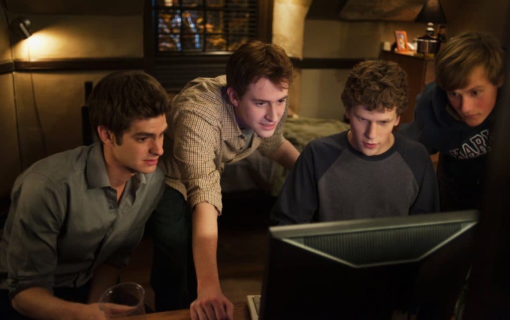 A group of guys look around a computer screen in The Social Network