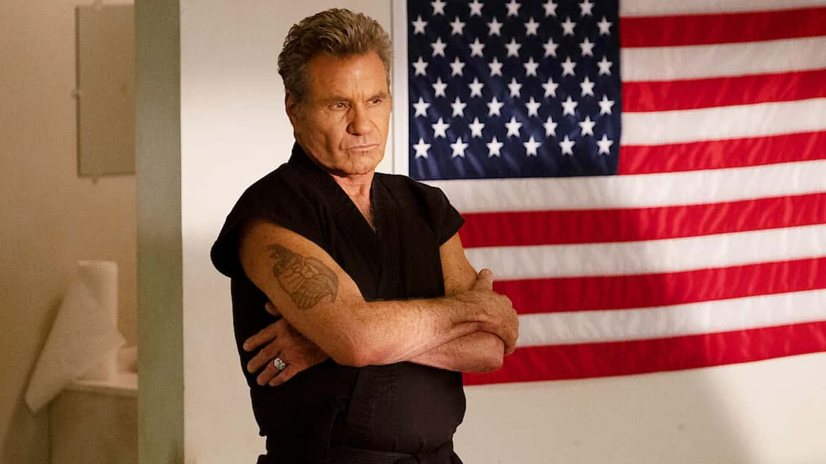 John Kreese standing in front of an American flag in Cobra Kai.